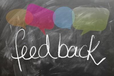 The word "feedback" is written on a chalkboard with colorful conversation bubbles surrounding it.